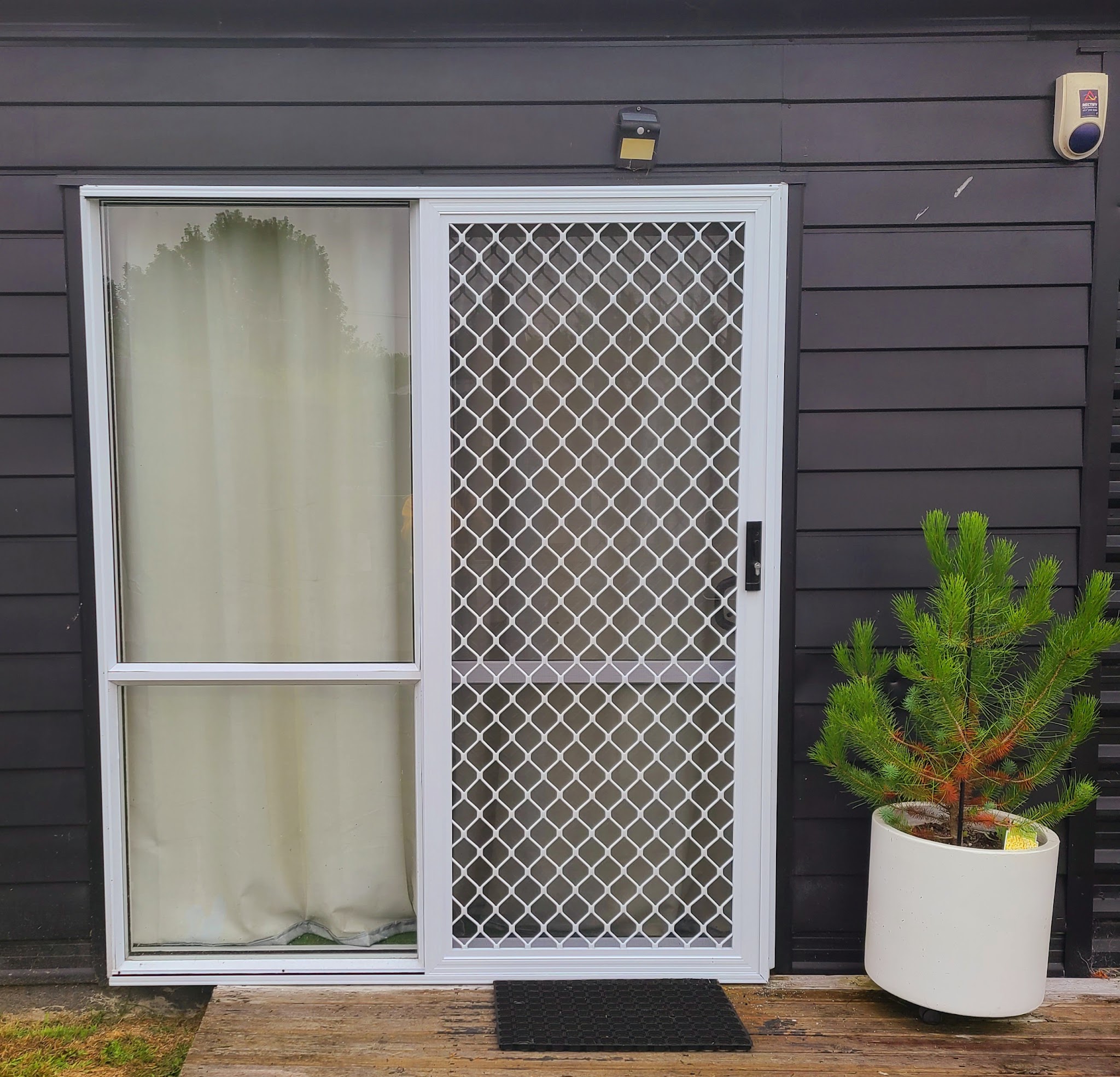 Sliding door with a white security mesh screen door on dark cladding